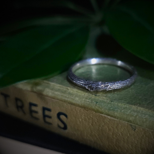 Sterling silver ring on a book titled 'TREES' with green leaves in the background.
The twig has deep longitudinal ridges and a knot in the centre.
