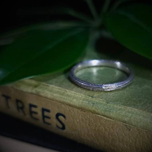 Sterling silver ring on a book titled 'TREES' with green leaves in the background.
The twig has deep longitudinal ridges on the outside and a smooth inside edge.
