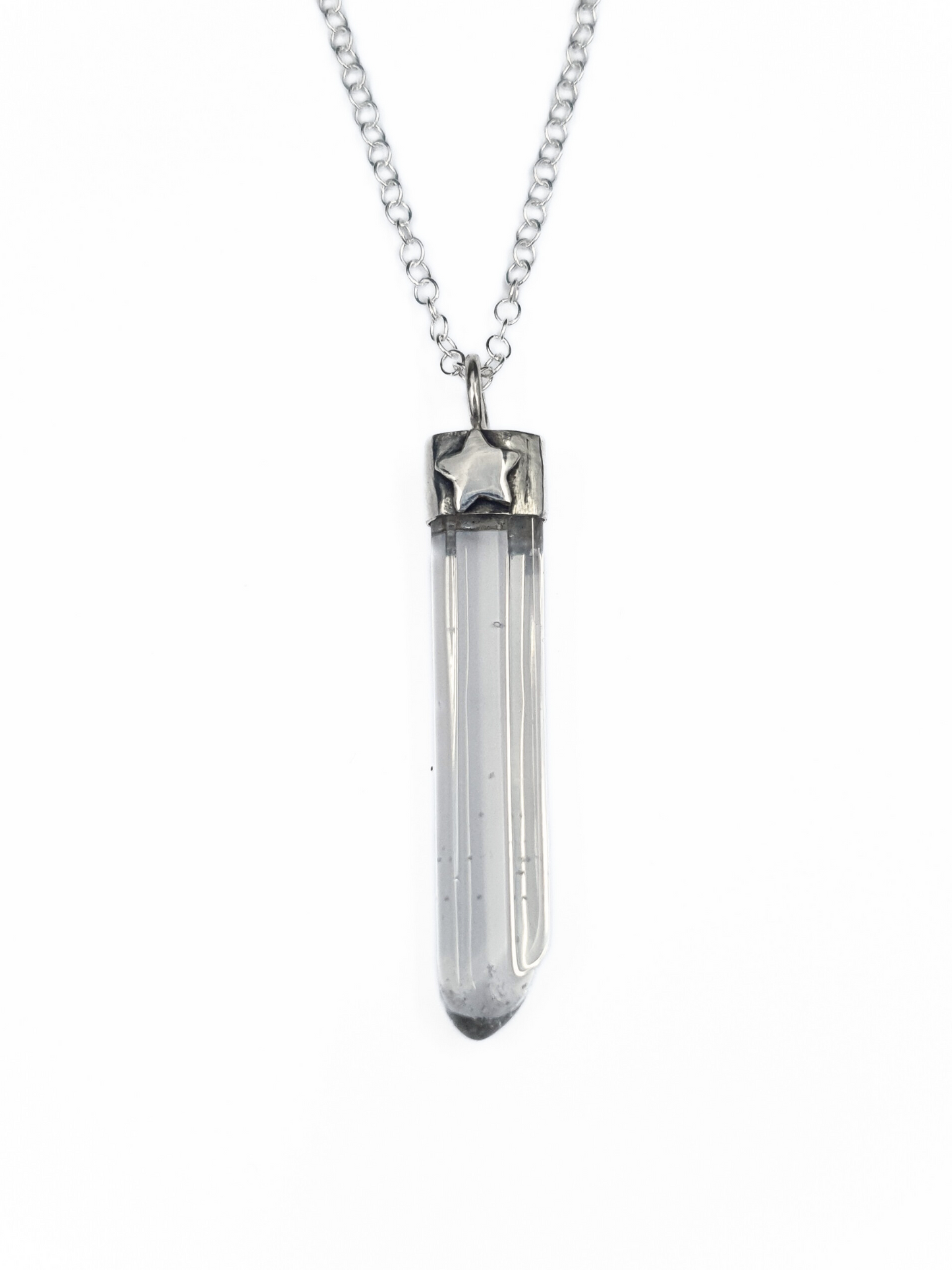 A silver pendant on a chain is displayed on a white background.
It is comprised of a long, thin, clear quartz point coming from a handmade silver setting.
It has a 3D silver star embellishment soldered to the front.