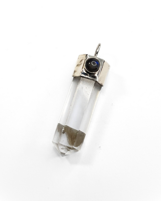 A clear quartz crystal point pendant with a sterling silver setting, adorned with a small labradorite stone, displayed against a white background.