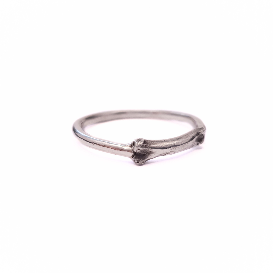 A silver ring sits against a plain white background. Part of the band of the ring is the solid silver casting of a little bone. The details are oxidised to show all the beautiful natural texture.