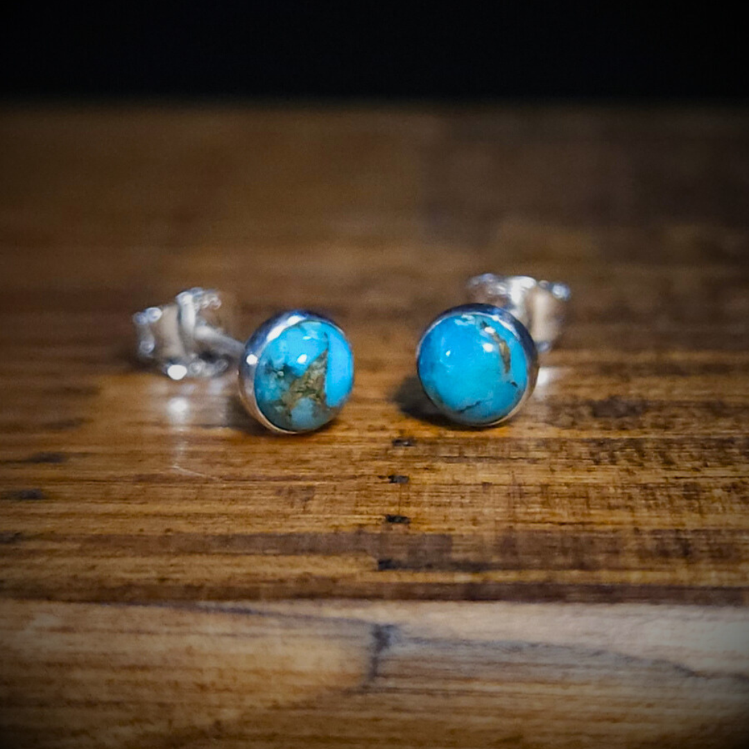 A pair of round sterling silver & blue copper turquoise it on a wooden surface.