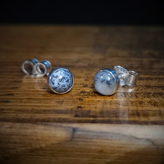 A pair of round sterling silver & monochrome dendritic agate gemstone stud earrings on a wooden surface