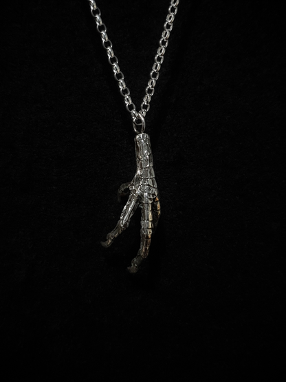 A solid silver casting of a pigeon claw hangs against a black background. This is a pendant and hung on a silver chain.
