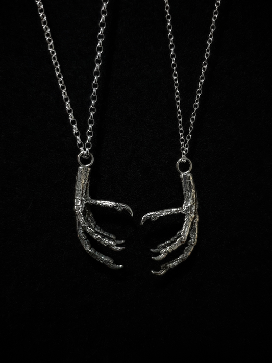 Two silver pendants, displayed on a thin trace and thick belcher chain for size comparison, hang against a black background.
The pendants are solid silver castings of pigeon claws at their real size.