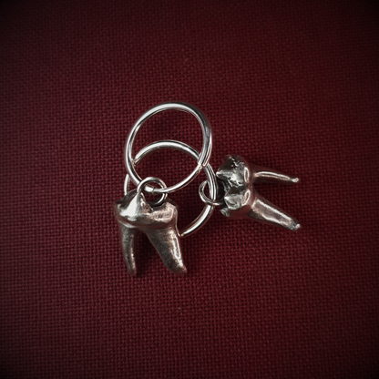 Two sterling silver fox tooth hoop earrings lay arranged on top of one another on a red-wine burgundy cloth background