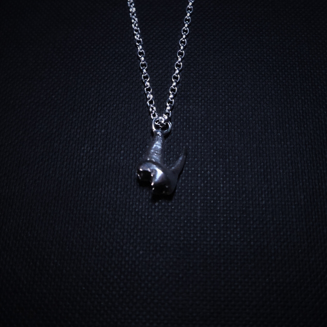 A tiny solid silver fox tooth hangs on a pendant against a black background