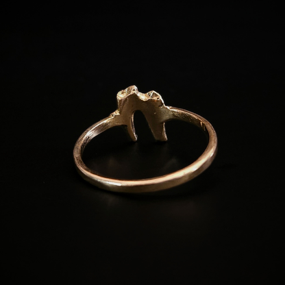 A dainty but luxurious, alt style, solid gold ring made using the casting of a real baby fox tooth, sits against the black background, photographed from the back to show that the inside of the ring is smooth for a comfortable wear. This lovely ring is perfect for fans of a witchy and gothic aesthetic and fans of folklore and natural history.