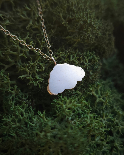A shiny, solid gold cloud pendant is strung on a lightweight gold chain and laid on a bed of rich green moss.