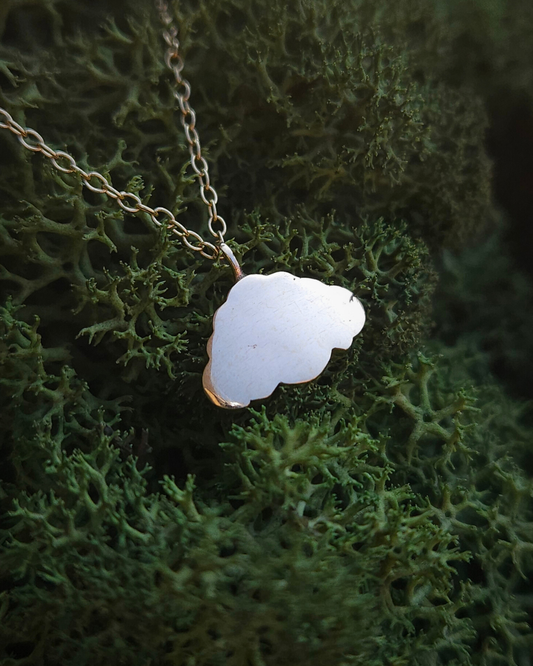 A shiny, solid gold cloud pendant is strung on a lightweight gold chain and laid on a bed of rich green moss.