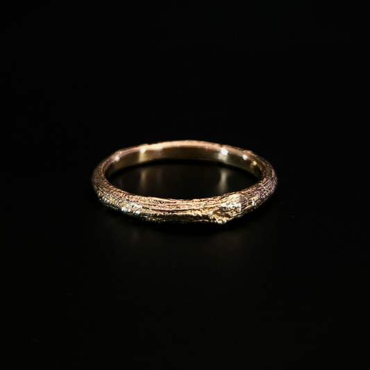 A richly-textured, 9 carat gold ring with an  organic bark-like surface, photographed on a solid black background. The inside of the ring is smooth for comfort and light is reflecting beautifully from the whole ring.