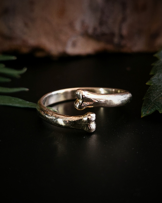 A 9 carat yellow gold open ring with two bone-shaped ends, photographed on a black surface with a natural background. The ring reflects a luxurious warn glow.