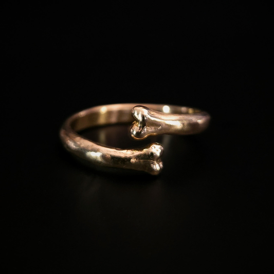 A 9 carat yellow gold open ring with two bone-shaped ends, photographed on a solid black background. The ring reflects a luxurious warn glow.