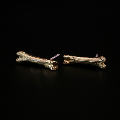 A pair of witchy 9 carat gold bone stud earrings laying on their side on a solid black background.