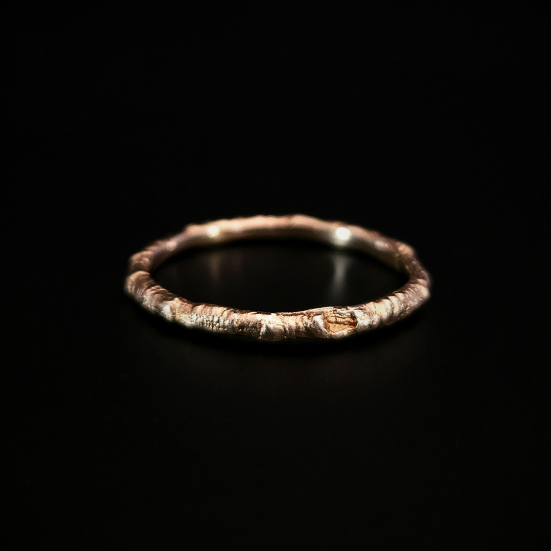 A 9 carat yellow gold ring made from the casting of a thin twig sits on a black surface. The inside of the ring is nice and smooth for comfort and the light reflects from it in a soft warm glow.