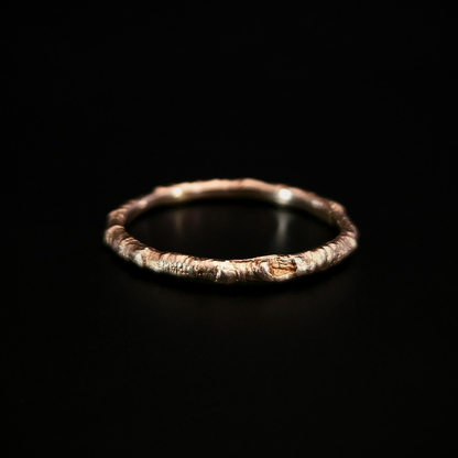 A 9 carat yellow gold ring made from the casting of a thin twig sits on a black surface. The inside of the ring is nice and smooth for comfort and the light reflects from it in a soft warm glow.