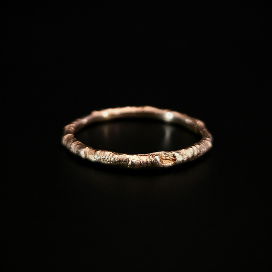 A 9 carat yellow gold ring made from the casting of a thin twig sits on a black surface. The inside of the ring is nice and smooth for comfort and the light reflects from it in a soft warm glow.