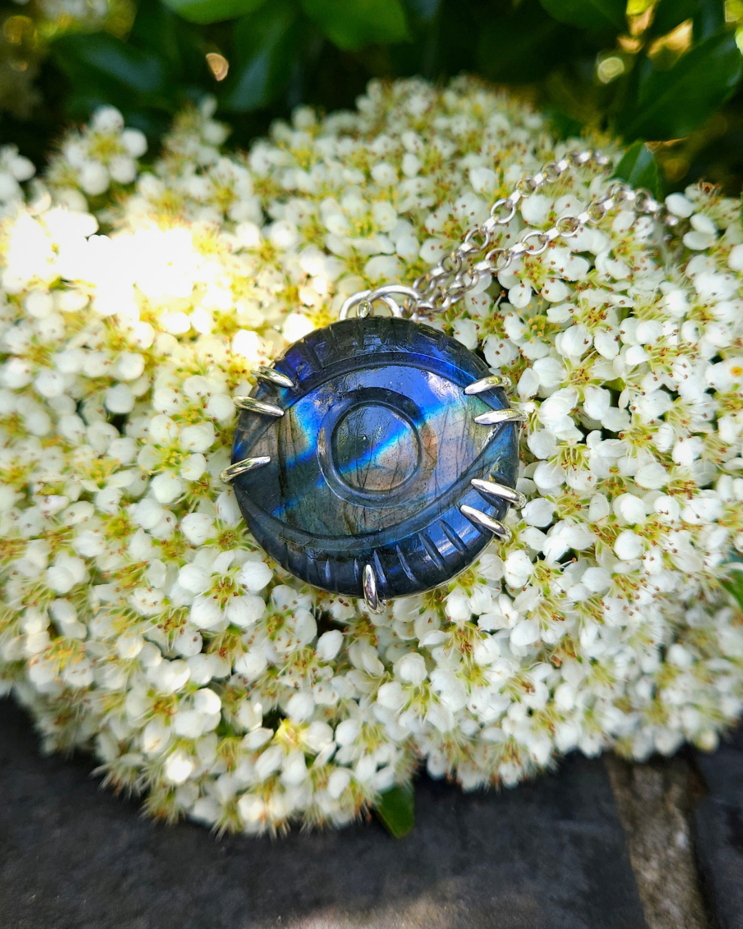 Blue Labradorite & sterling silver necklace on white flowers with green leaves. The labradorite has an eye carved into it and displays lovely flashes of colour on the surface. The .925 sterling silver pendant has gently pointed claws.