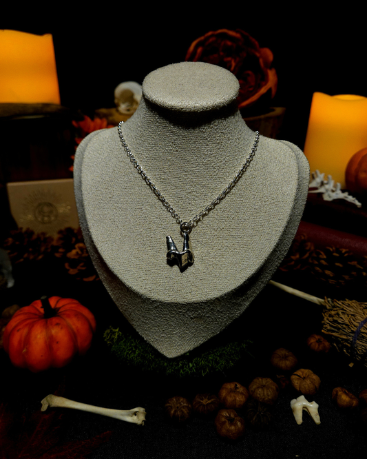 A silver chain necklace with a solid silver fox tooth pendant displayed on a cream jewellery bust. The photograph is styled in a gothic, moody setting with candles, pumpkins, bones, and autumnal botanicals around it.