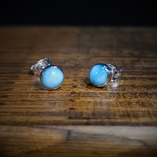 A pair of round blue larimar & sterling silver stud earrings on a wooden surface