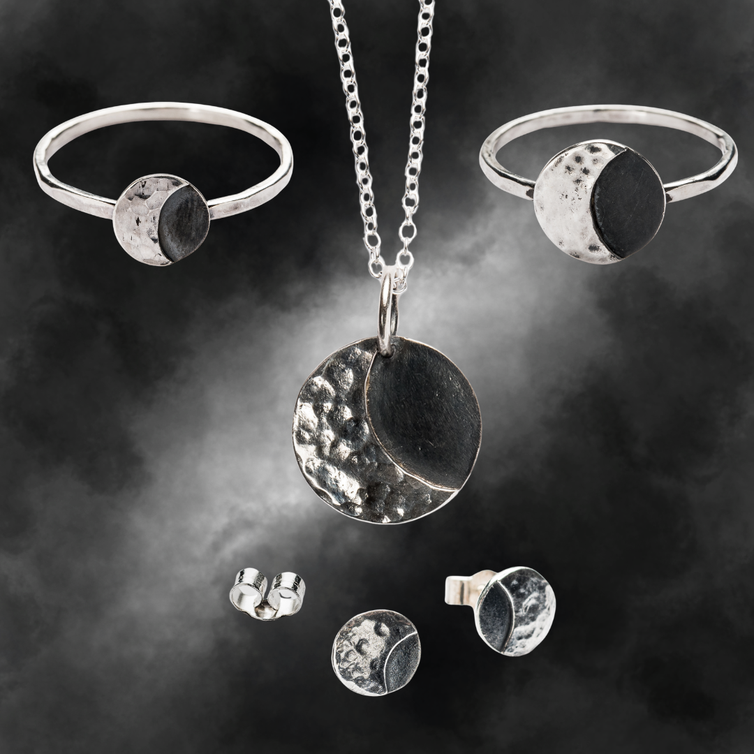 A set of lunar sterling silver jewellery including 2 rings, a pair of stud earrings, and a necklace, featuring a textured and smooth finish with a moon motif.