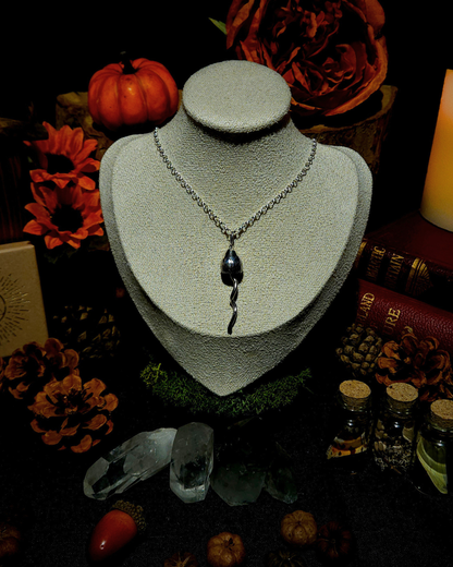 A silver chain with a solid silver magic mushroom pendant displayed on a vintage style cream jewellery bust. The photograph is styled in a witchy, moody setting with candles, pumpkins, bones, & other autumnal botanicals around it.
