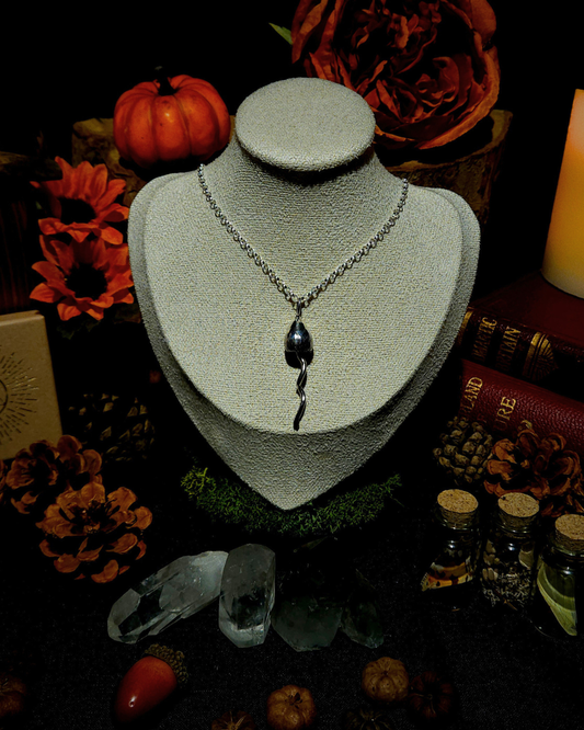 A silver chain with a solid silver magic mushroom pendant displayed on a vintage style cream jewellery bust. The photograph is styled in a witchy, moody setting with candles, pumpkins, bones, & other autumnal botanicals around it.