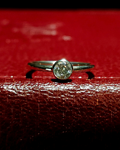A sterling silver and moissanite solitaire ring laying on its side, stone facing towards the camera, sparkling brightly. It lays on a dark red, vintage book.