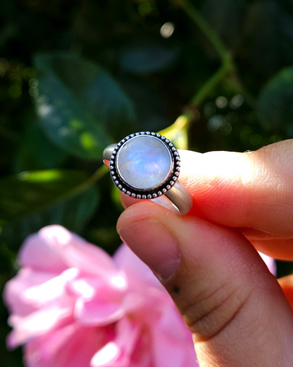 A sterling silver and round rainbow moonstone held by a hand against a blurred natural background. An etherial, blue, luminescence is visible in the high quality, ethically sourced stone.