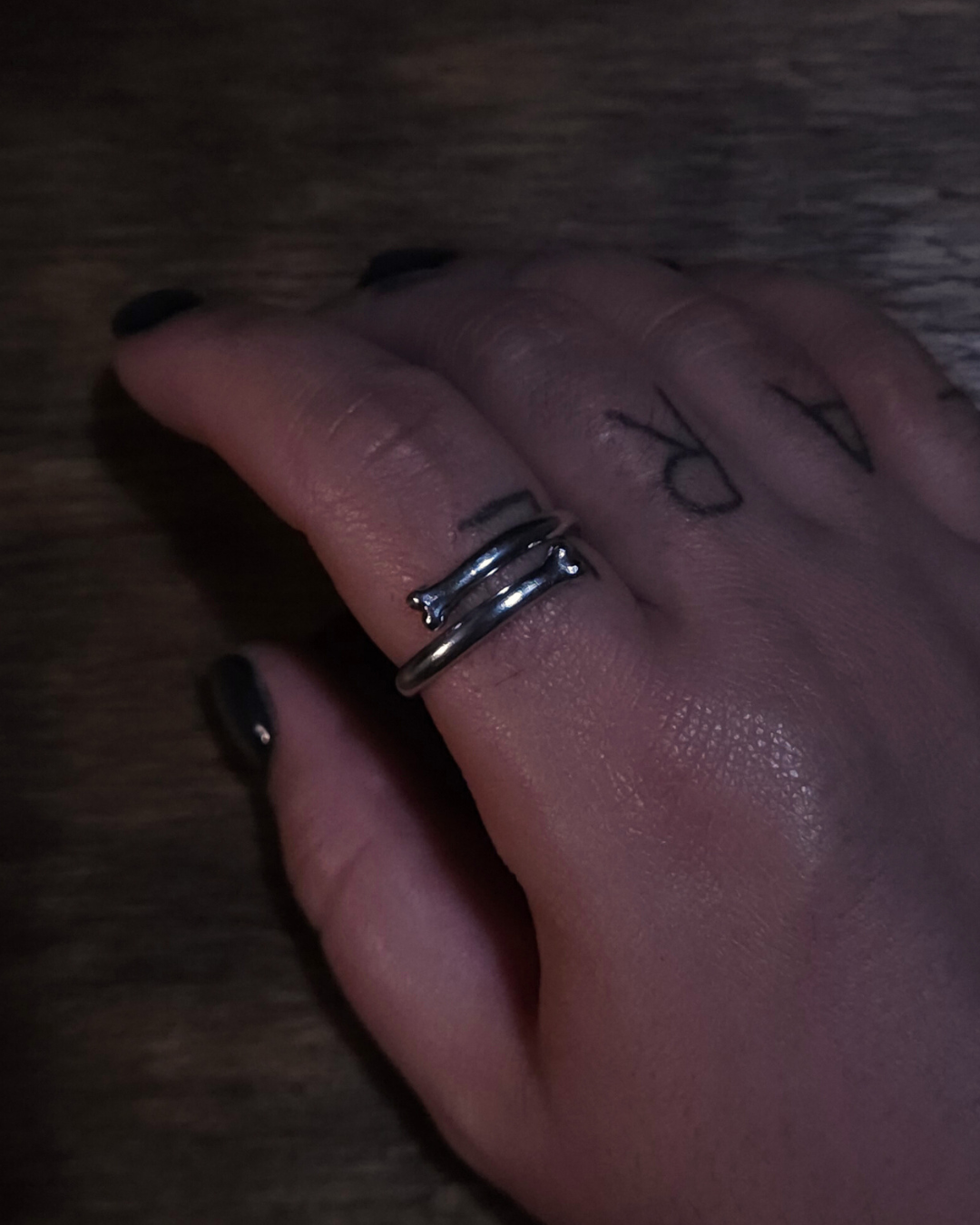 A hand wears an open style bone ring in sterling silver on their forefinger