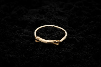 A luxury, gothic, yellow 9 caratt gold ring ring lays on black sand. Part of the band of the ring is the solid gold casting of a little bone