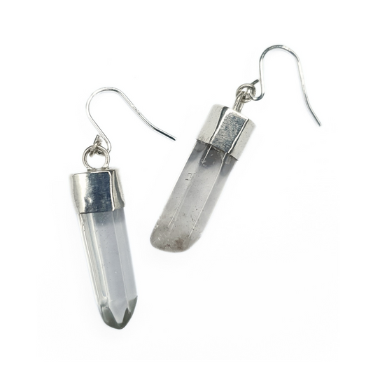 A pair of quartz and silver earrings are displayed on a white background.
They are comprised of a clear quartz point coming from a handmade silver setting with a silver hook. 