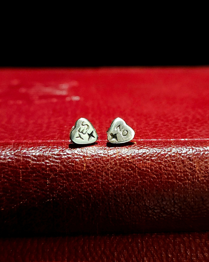 A pair of small, .925 silver ouija planchette stud earrings sit on a vintage red book with a black background. The earring on the left says "YES" and the one on the right says "NO" and they both have a 4-pointed star at the bottom of each pointer.