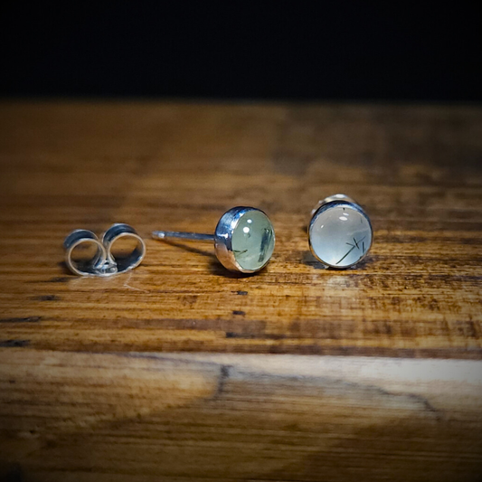 A pair of round sterling silver & prehnite stud earrings on a wooden surface