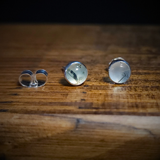 A pair of round sterling silver & prehnite stud earrings on a wooden surface