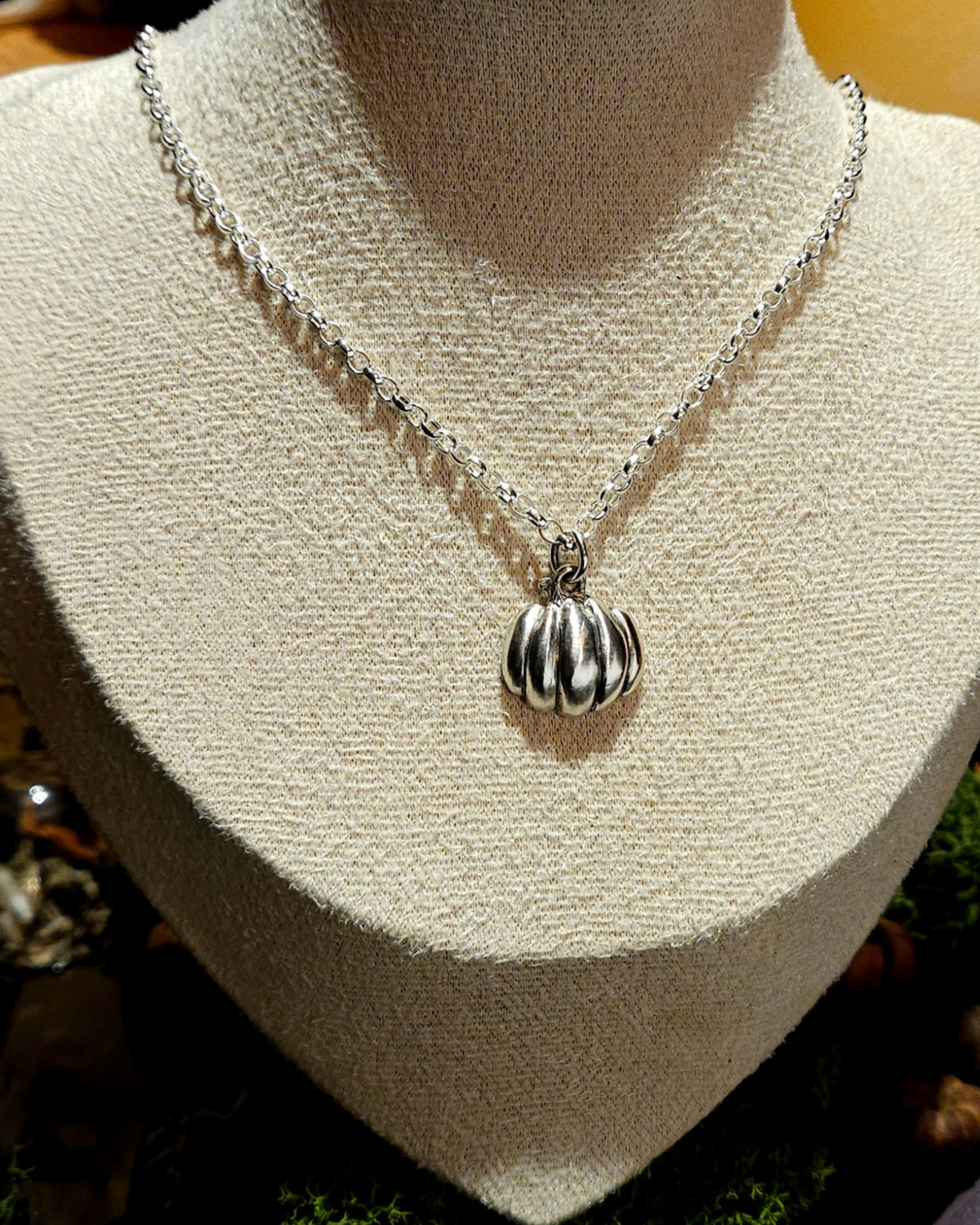 A close-up picture of a solid silver halloween pumpkin pendant displayed on a vintage beige jewellery bust.