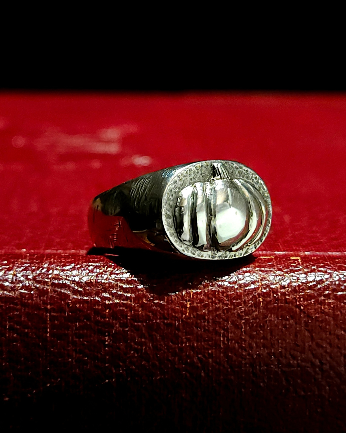 A thick solid silver signet ring with 3D pumpkin detailing, displayed on a textured vintage red book. It is oxidised to reveal detailing and polished back to a bright shine.