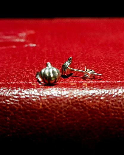 A pair of .925 silver pumpkin stud earrings sit on a vintage red book. The one on the right is facing forward and out of focus, the one on the right is in focus, and facing sideways to show its flat back and butterfly fastener.
