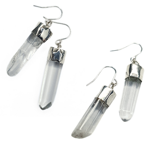 Two pairs of quartz and silver earrings are displayed on a white background.
They are both comprised of a clear quartz point coming from a handmade silver setting with a silver hook. 
The pair on the left has a 3D silver star embellishment on the front of each silver setting.