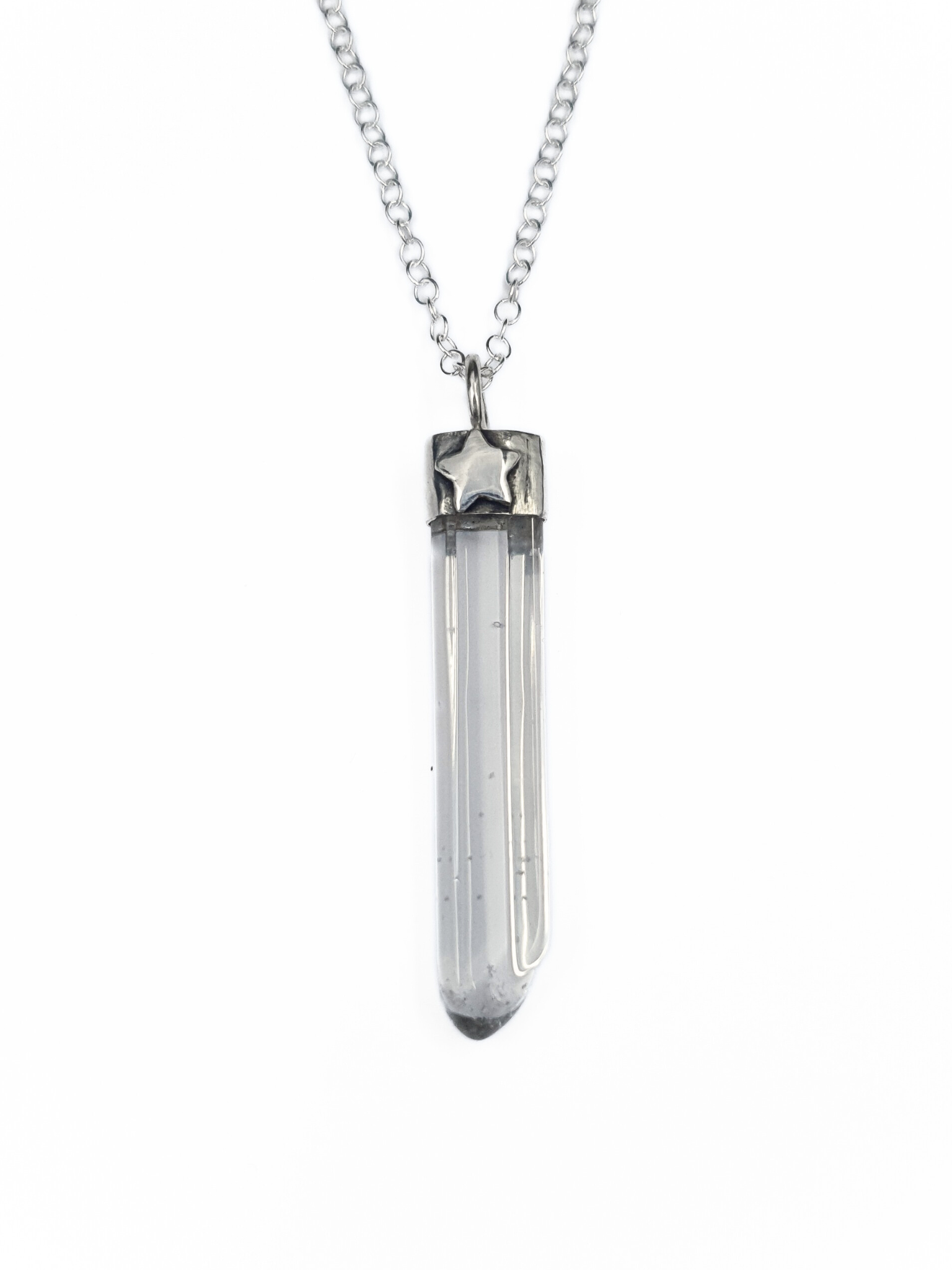 A silver pendant on a chain is displayed on a white background.
It is comprised of a long, thin, clear quartz point coming from a handmade silver setting.
It has a 3D silver star embellishment soldered to the front.