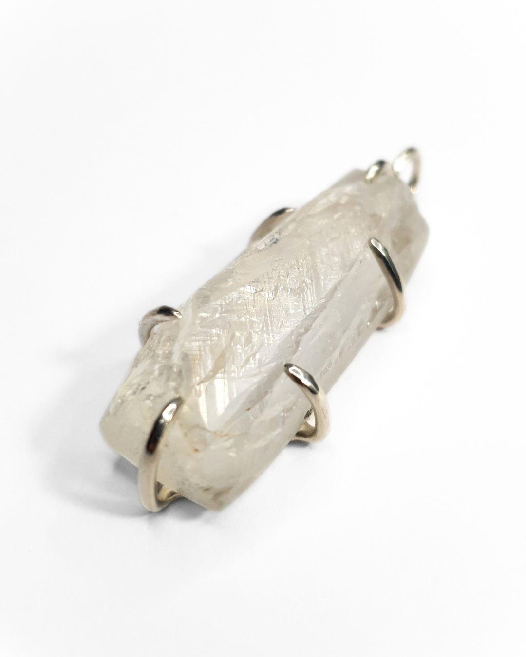 A rough-cut, rectangle-shaped quartz is photographed on a white background. The rough, beautifully textured stone is set in 6 silver claws - 1 and the top and bottom and two on each side. A silver jump ring is visible at the top.