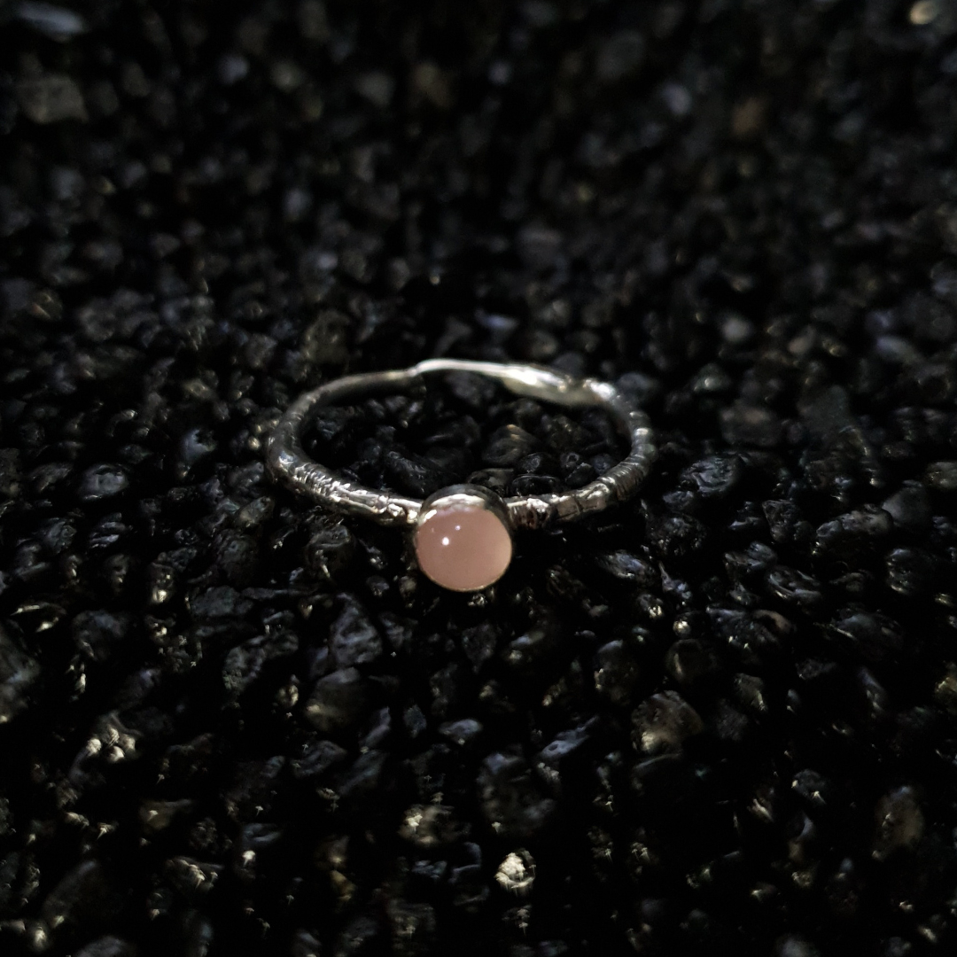 Silver ring with a 5mm rose quartz gemstone on a black textured background. The band is made from the casting of a real twig so it is full of bark texture. The rose quartz has a gentle light pink blush.