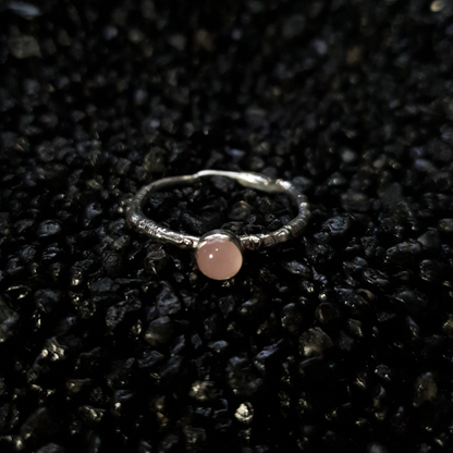 Silver ring with a 5mm rose quartz gemstone on a black textured background. The band is made from the casting of a real twig so it is full of bark texture. The rose quartz has a gentle light pink blush.