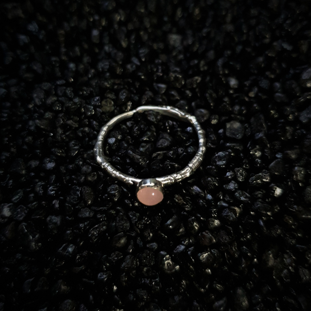 Silver ring with a 5mm rose quartz gemstone on a black textured background. The band is made from the casting of a real twig so it is full of bark texture. The rose quartz has a gentle light pink blush.