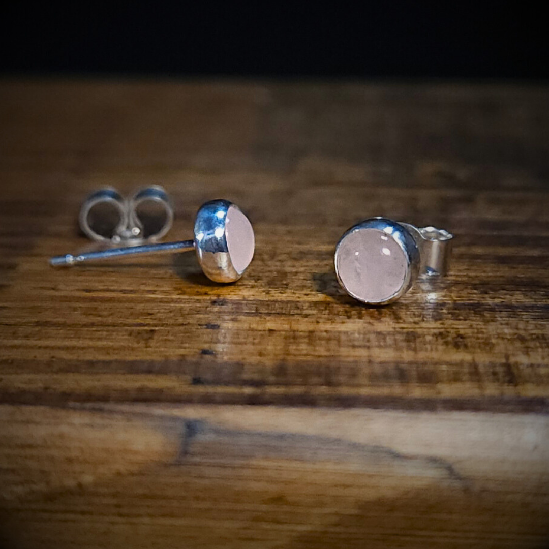 A pair of round sterling silver & rose quartz stud earrings on a wooden surface
