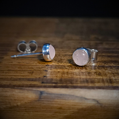 A pair of round sterling silver & rose quartz stud earrings on a wooden surface