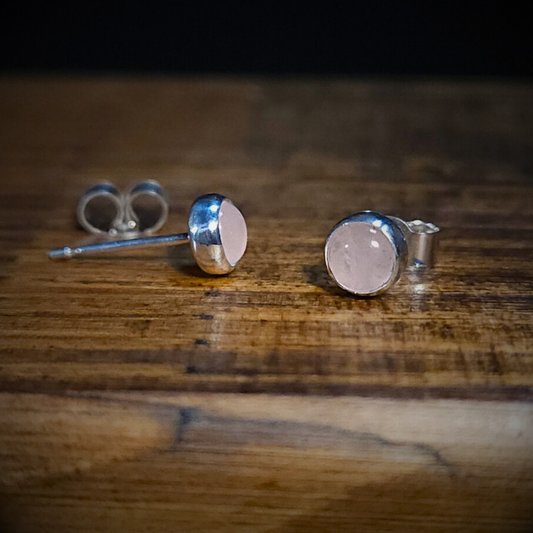 A pair of round sterling silver & rose quartz stud earrings on a wooden surface
