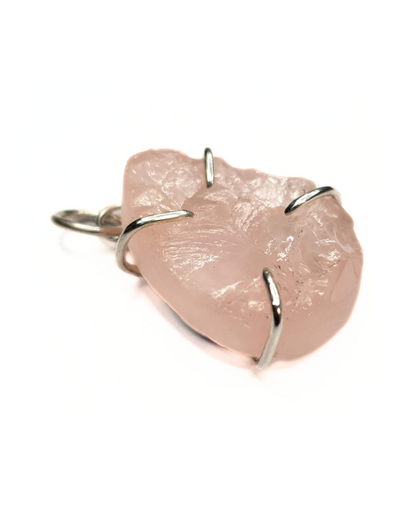 A rough-cut, semi-transparent, teardrop-shaped rose quartz pendant is photographed on a white background. The rough, beautifully textured stone is set in 4 evenly spaced silver claws. A silver bail is at the top with a silver jump ring through it.