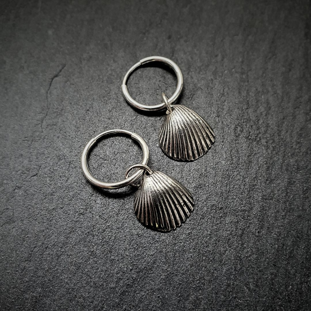 A cute pair of .999 fine silver shell hoops sit on a grey slate slice.