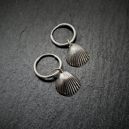A cute pair of .999 fine silver shell hoops sit on a grey slate slice.